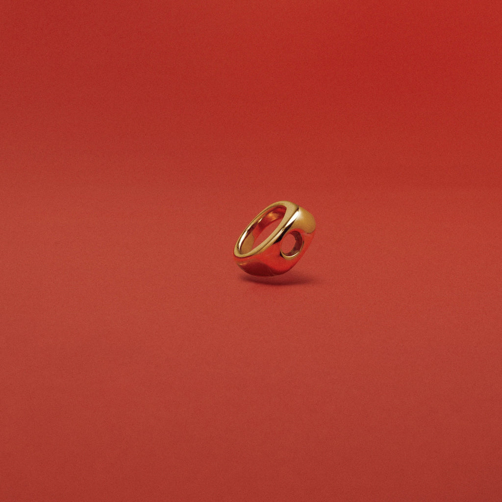 A small gold ring with a circular cutout, standing upright on a solid red background.