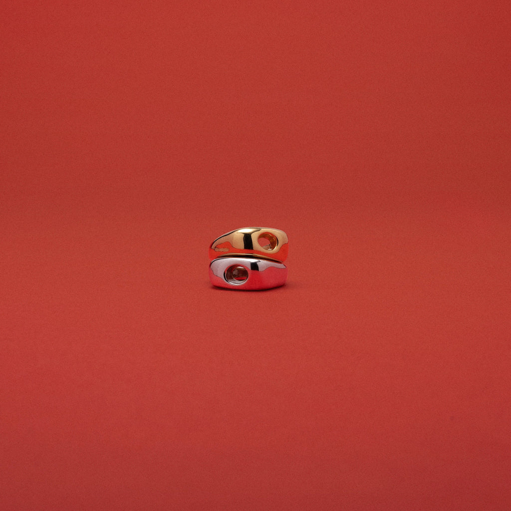 A small gold ring with a white enamel inlay and a red center detail, photographed against a solid red background.