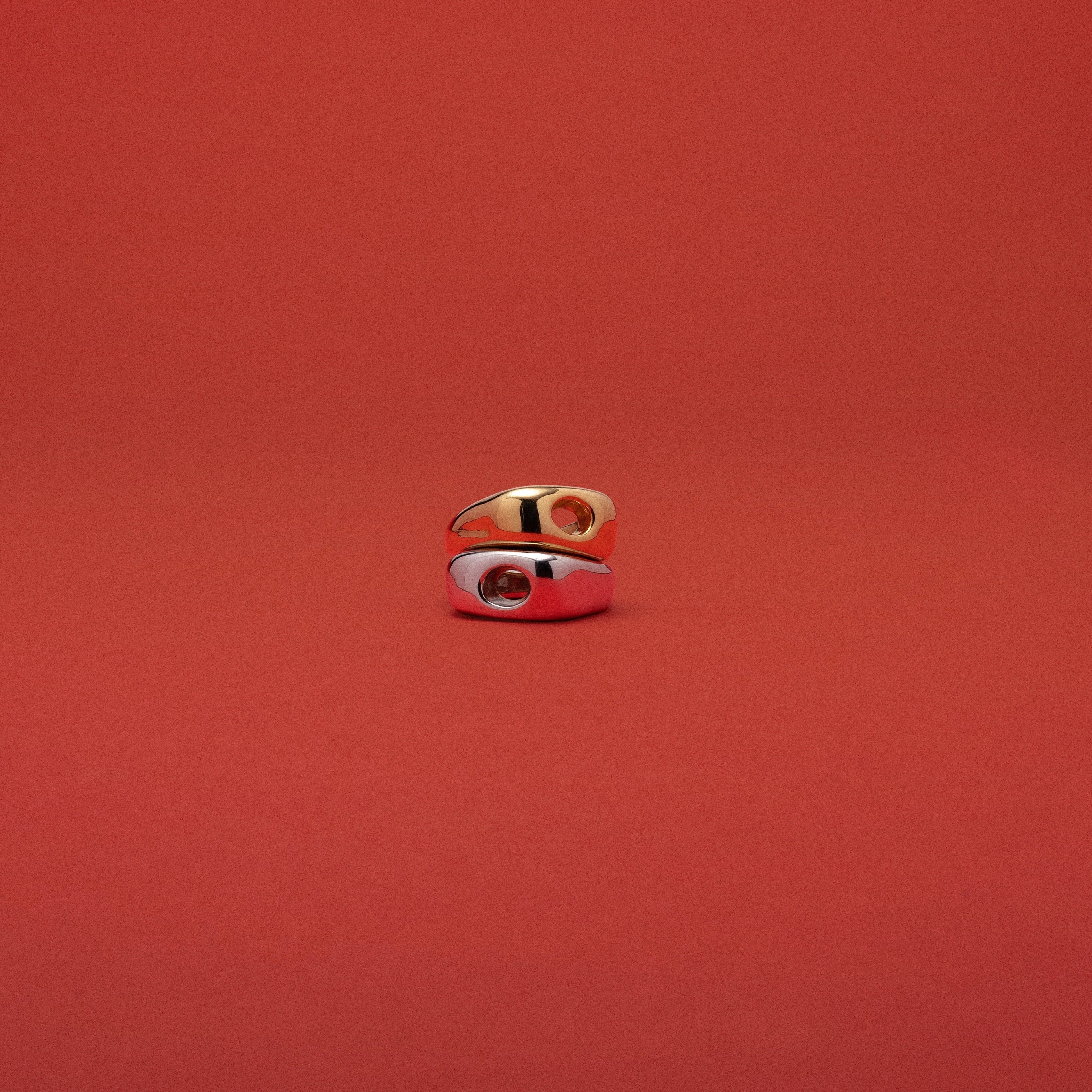 A small gold ring with a white enamel inlay and a red center detail, photographed against a solid red background.