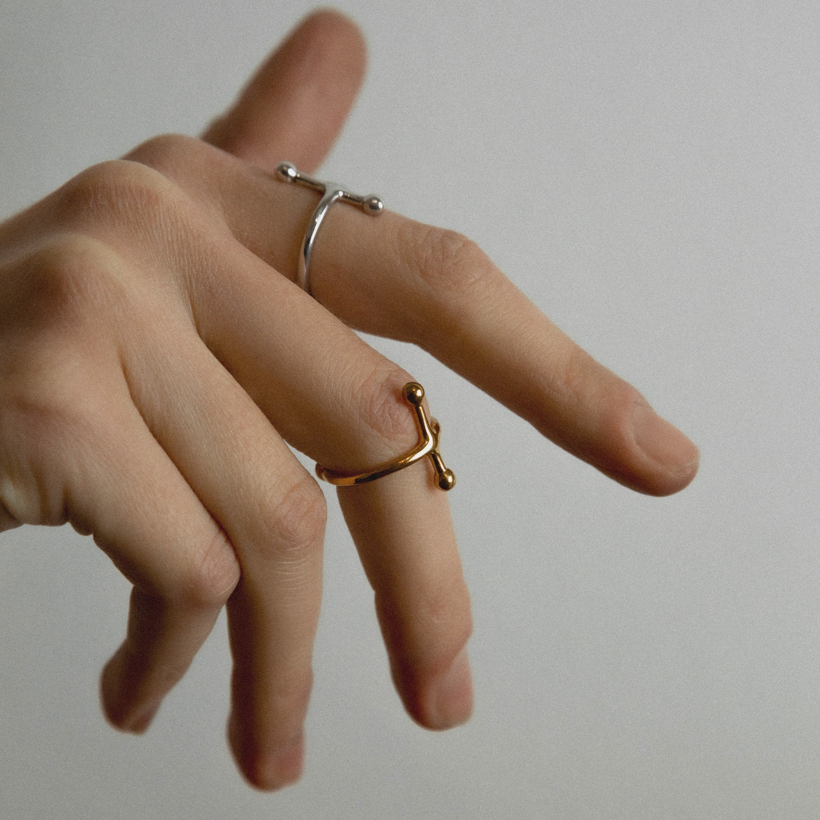 Hand wearing two rings on a plain background