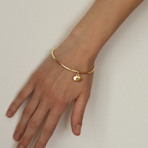 Gold bracelet with a heart charm on a wrist against a plain background